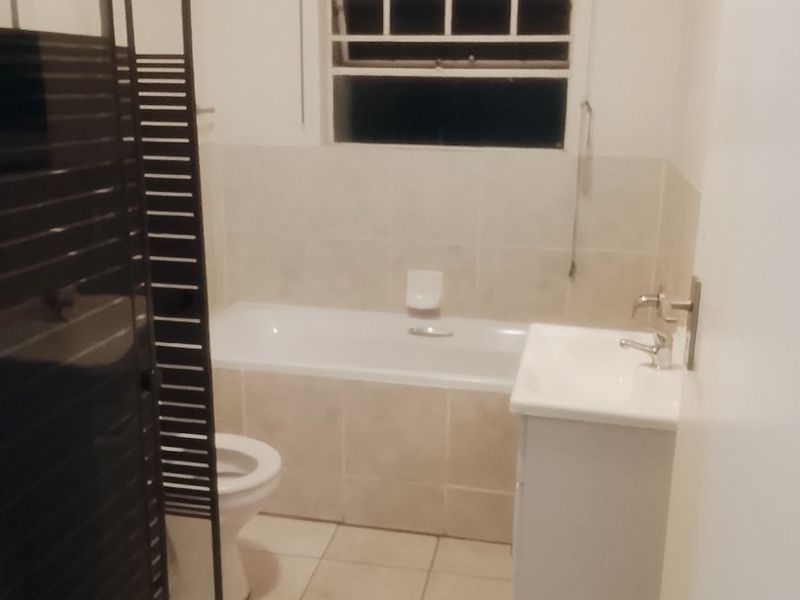 A functional bathroom featuring a bathtub, shower enclosure, vanity basin, and toilet with neutral tiled finishes.