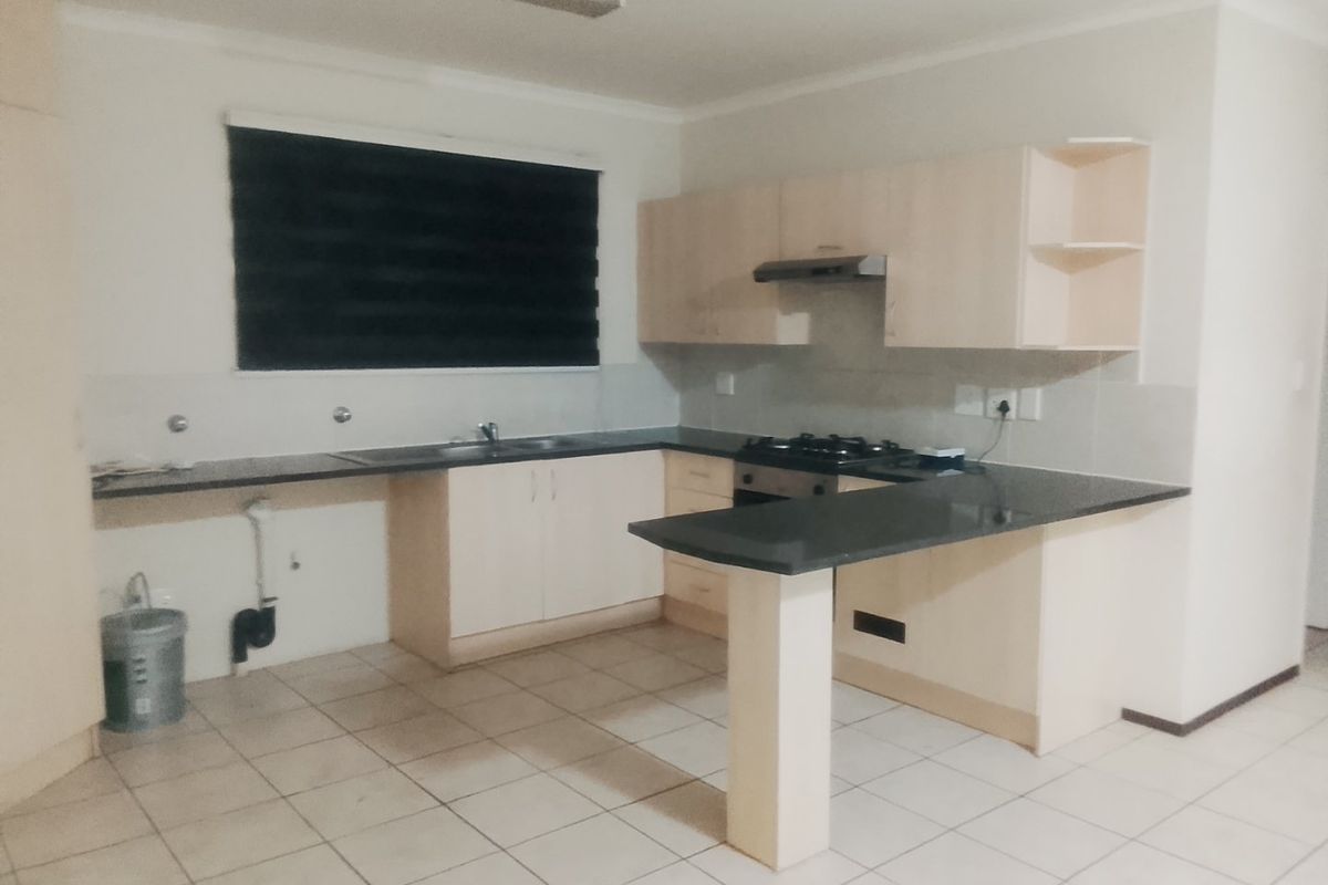 A functional kitchen featuring light-toned cabinetry, dark granite countertops, a gas hob with extractor, and tiled flooring in an open-plan layout.