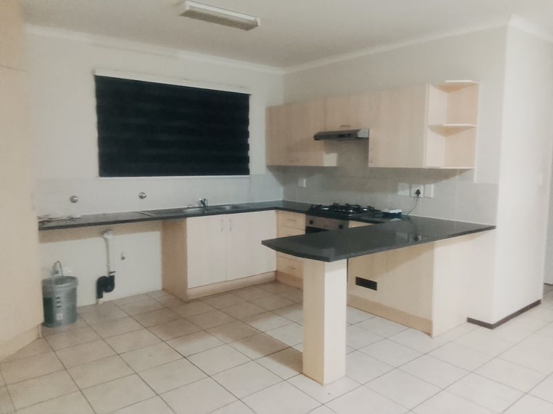 A functional kitchen featuring light-toned cabinetry, dark granite countertops, a gas hob with extractor, and tiled flooring in an open-plan layout.