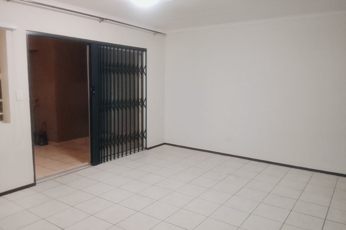 An empty living room featuring white tiled flooring and a sliding security gate leading to an outdoor area.