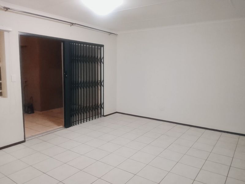 An empty living room featuring white tiled flooring and a sliding security gate leading to an outdoor area.