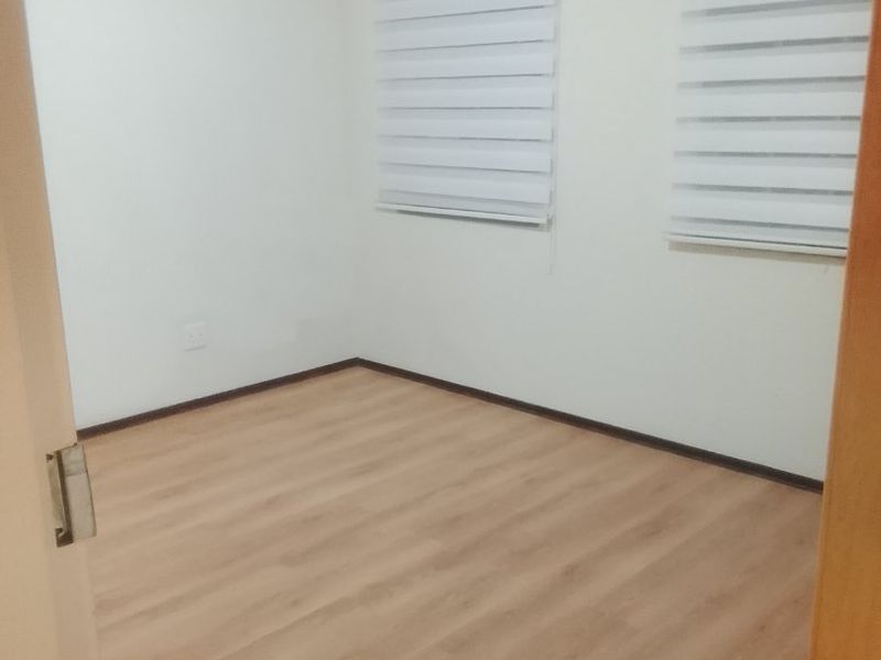 A clean, empty bedroom featuring light wood-look laminate flooring, neutral white walls, and modern roller blinds.