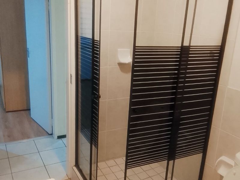 A functional bathroom featuring a corner shower enclosure with black frame detailing, tiled walls, a toilet, and a vanity basin.