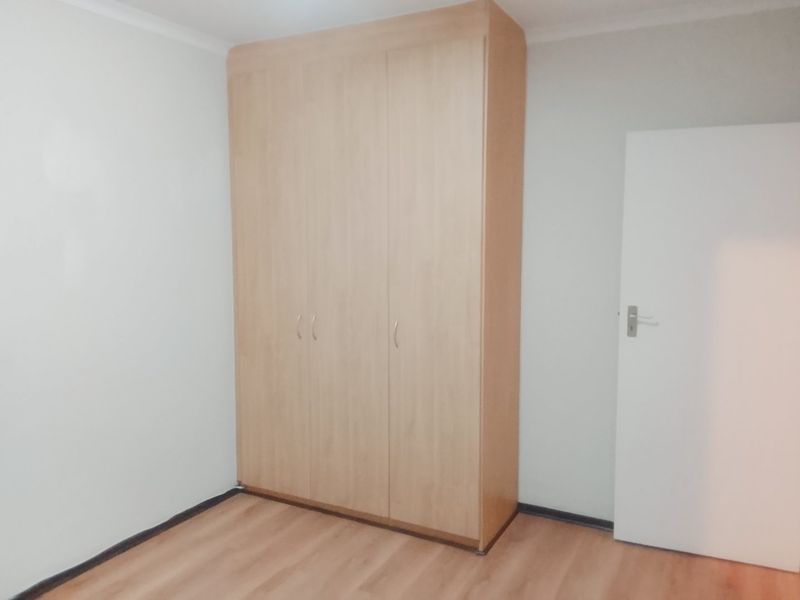 A clean, empty bedroom featuring light-toned laminate flooring and a large built-in wooden wardrobe.