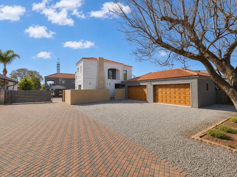 Front exterior view of the property featuring a paved and gravel driveway, double garage, and secure boundary walling.