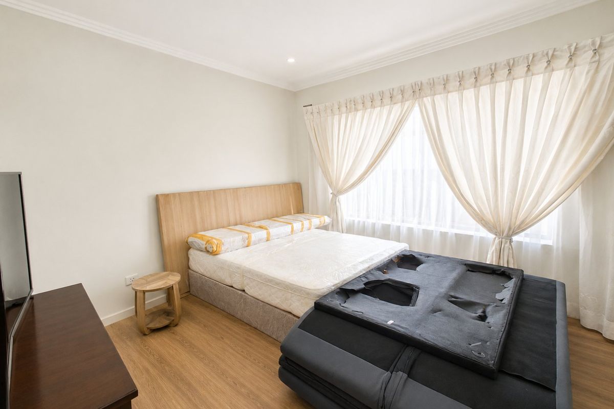A well-lit bedroom featuring light-toned laminate flooring, recessed downlighting, and decorative cove cornicing.