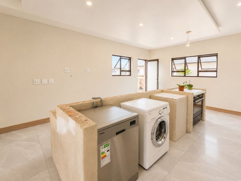 A bright, open-plan kitchen area featuring a unique masonry island structure, tiled flooring, and recessed lighting, ready for custom cabinetry or finishing.