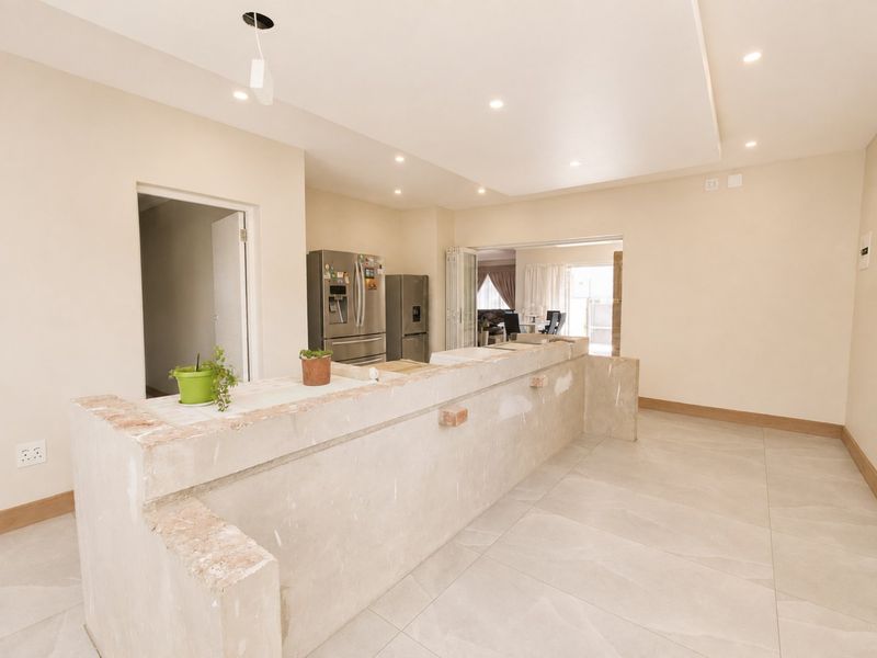Spacious kitchen area featuring large format floor tiles, recessed lighting, and a substantial stone breakfast bar currently in an unfinished state.