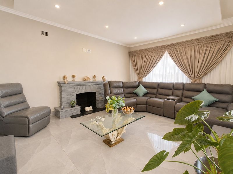 Spacious living room featuring large format floor tiles, a stone fireplace, and recessed downlighting, creating a comfortable and well-maintained living space.