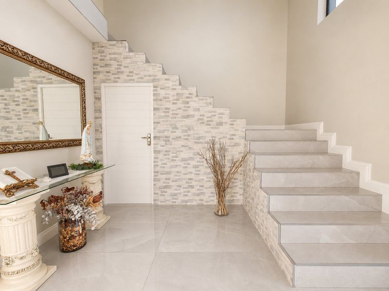 A bright and modern entrance hall featuring a tiled staircase, stone veneer accent wall, and polished floor tiles.