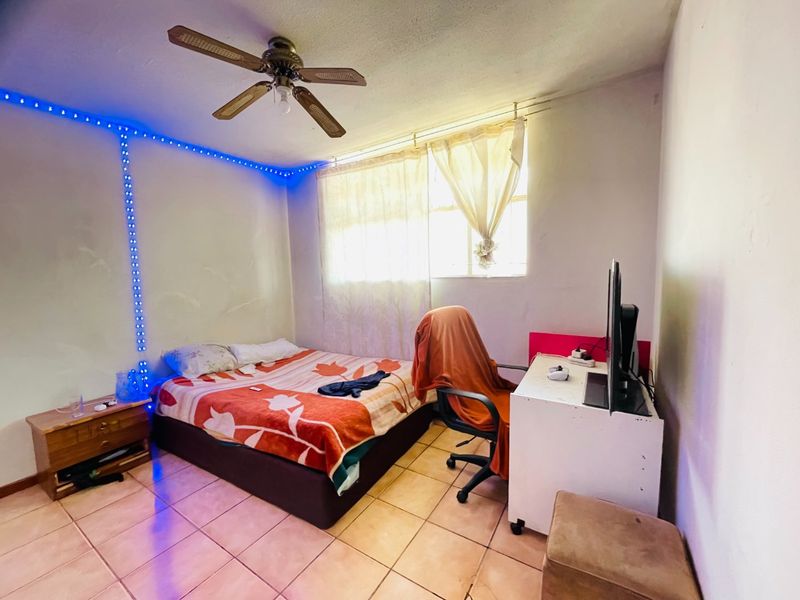 A bedroom featuring tiled flooring and a ceiling fan, providing a functional space with natural light from the window.