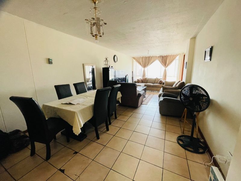 Open-plan living and dining area featuring ceramic floor tiles and natural light from large windows.