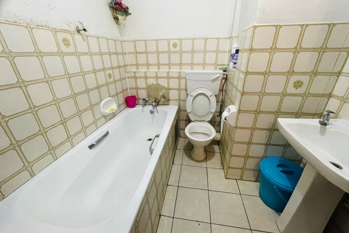 A dated bathroom featuring a standard bathtub, pedestal basin, and toilet with original tiled finishes requiring renovation and repair to the wall plaster.