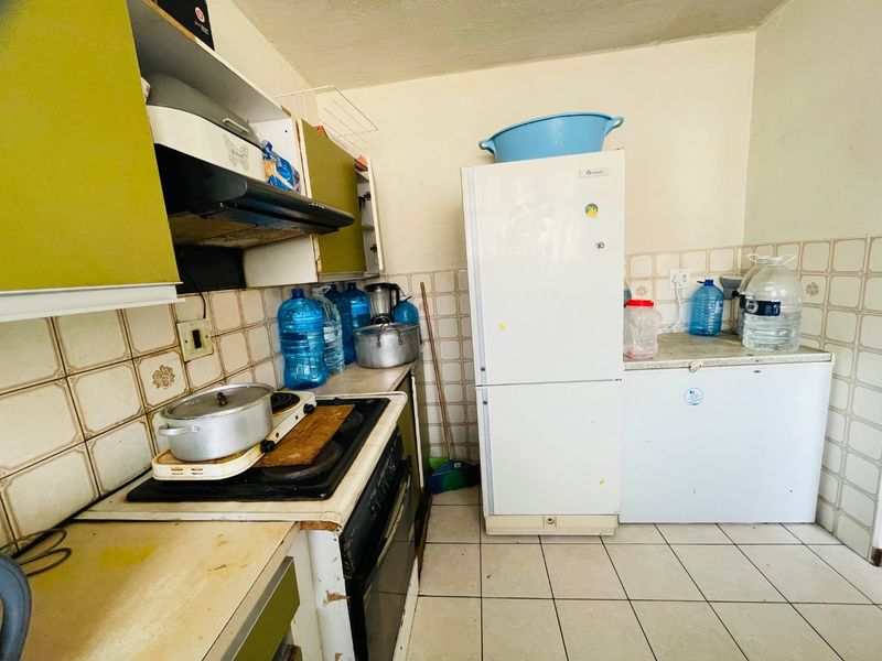 A dated kitchen featuring original cabinetry, tiled backsplash, and ceramic flooring, offering potential for a modern renovation to enhance functionality and aesthetic appeal.