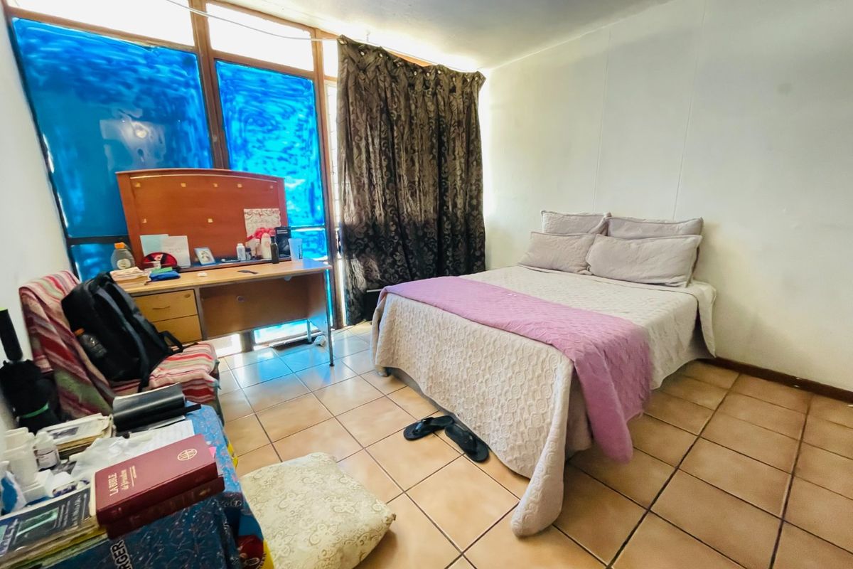 A bedroom featuring tiled flooring, a ceiling fan, and a large window with natural light, offering a functional space ready for cosmetic updates.