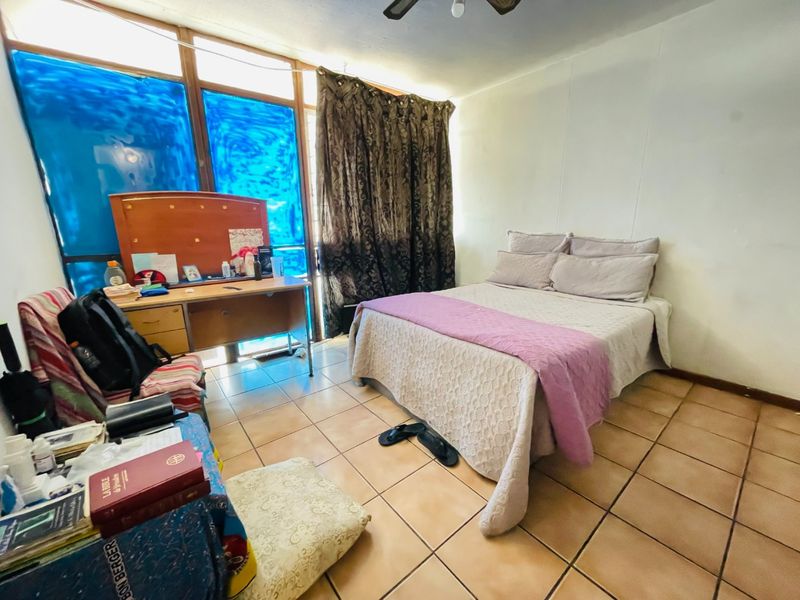 A bedroom featuring tiled flooring, a ceiling fan, and a large window with natural light, offering a functional space ready for cosmetic updates.