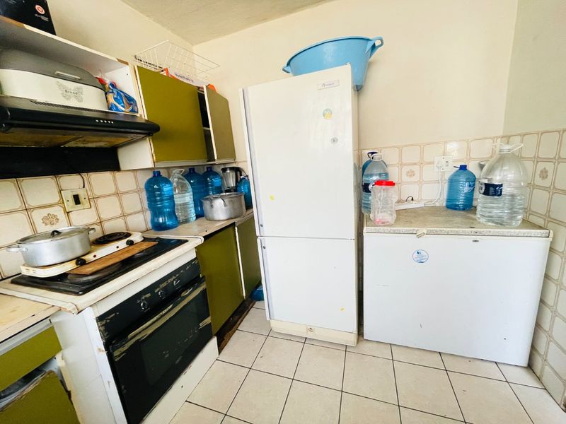 A compact kitchen featuring built-in cabinetry, an electric stove with extractor fan, and tiled backsplash, requiring cosmetic updates to improve its overall condition.