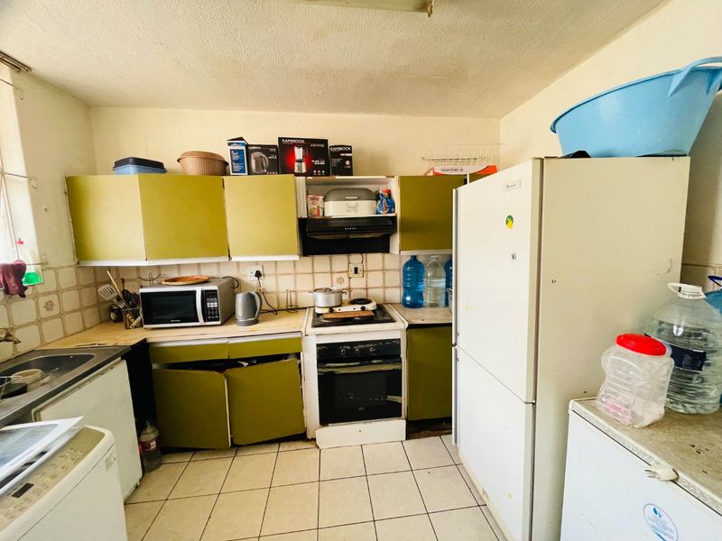 A dated kitchen featuring olive green cabinetry, tiled backsplash, and standard built-in appliances, requiring cosmetic updates to improve functionality and aesthetic appeal.