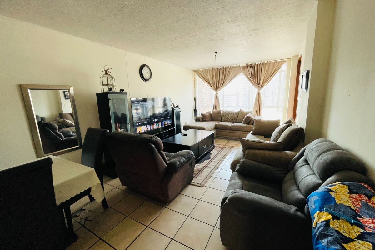 A spacious living room featuring ceramic floor tiles and a large window, offering a functional layout suitable for comfortable family living.
