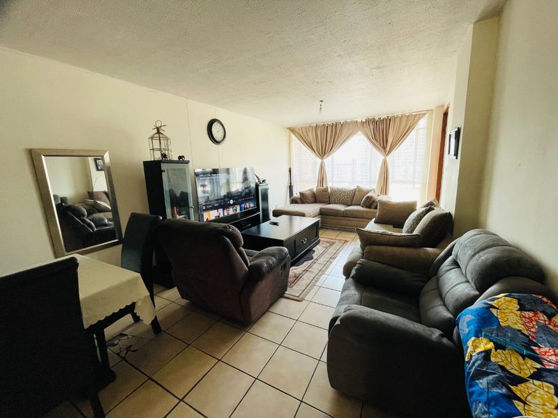 A spacious living room featuring ceramic floor tiles and a large window, offering a functional layout suitable for comfortable family living.