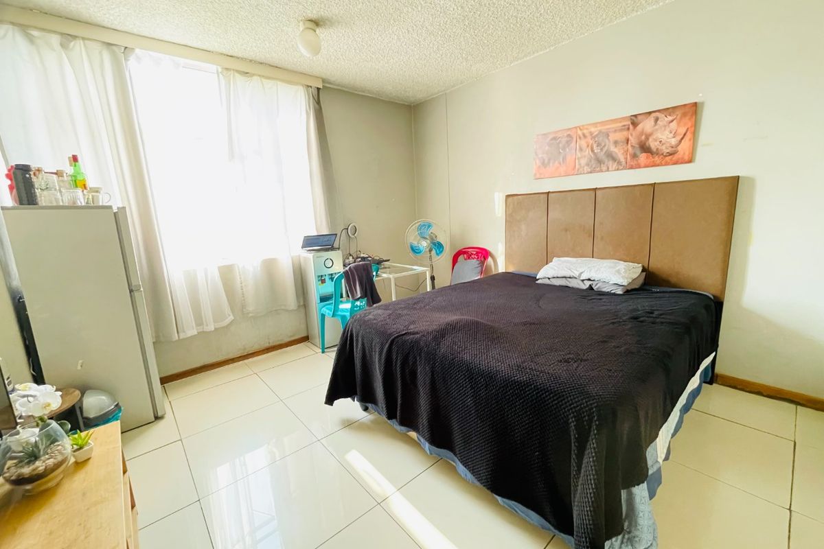 A bedroom featuring tiled flooring and a textured ceiling, offering a functional space with natural light from the window.