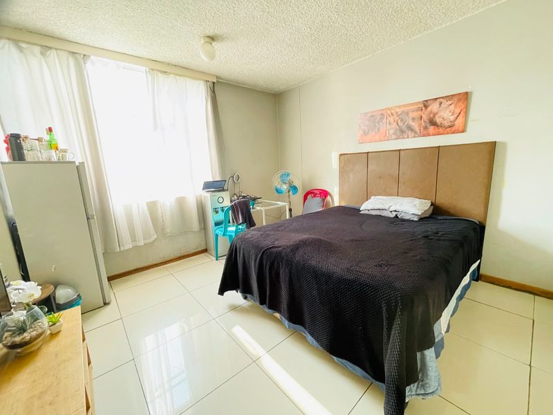 A bedroom featuring tiled flooring and a textured ceiling, offering a functional space with natural light from the window.