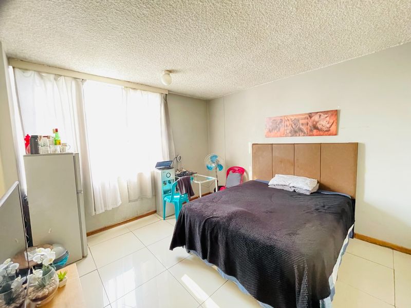 A bedroom featuring tiled flooring and a textured ceiling, offering a functional space with natural light from a large window.
