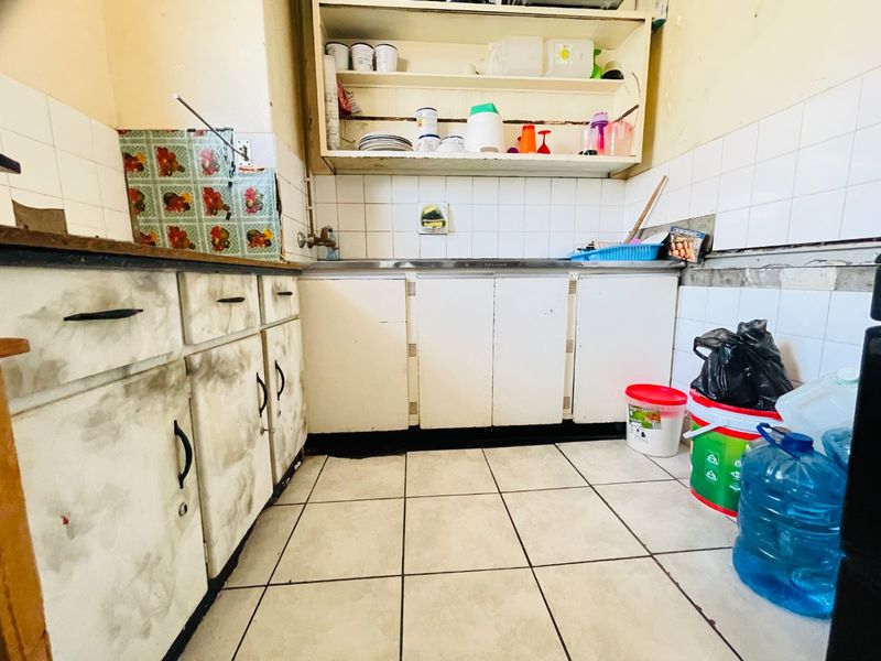 A dated kitchen featuring built-in cabinetry, a stainless steel sink, and tiled finishes, currently requiring significant maintenance and cosmetic updates.