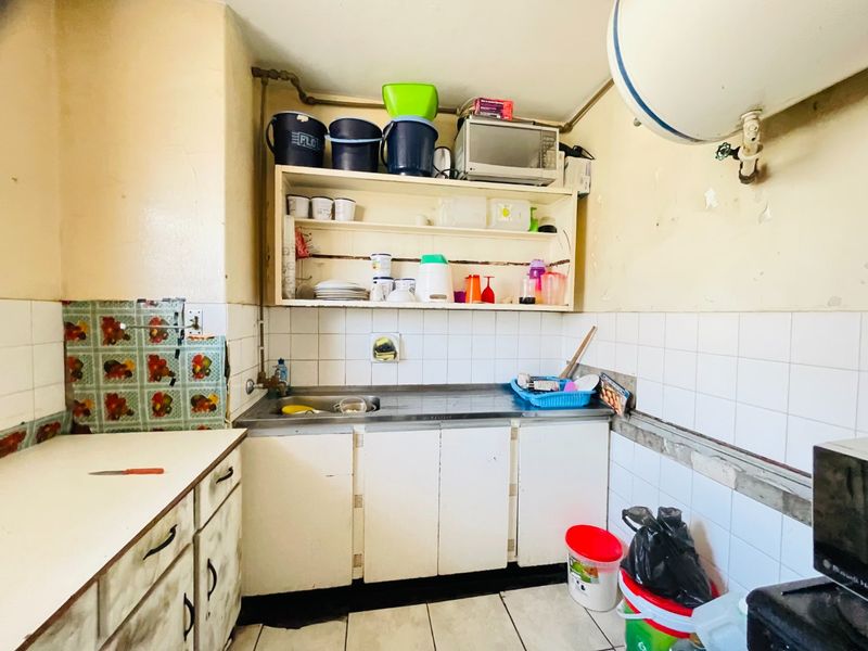 A compact kitchen area featuring a stainless steel sink, tiled backsplash, and built-in cabinetry, currently requiring significant maintenance and cosmetic updates.