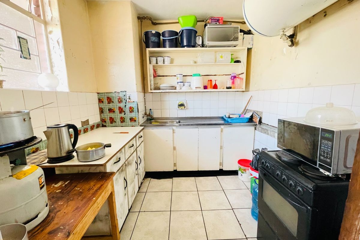 A compact kitchen featuring tiled flooring, a stainless steel sink, and built-in cabinetry, currently requiring significant cosmetic updates and maintenance.
