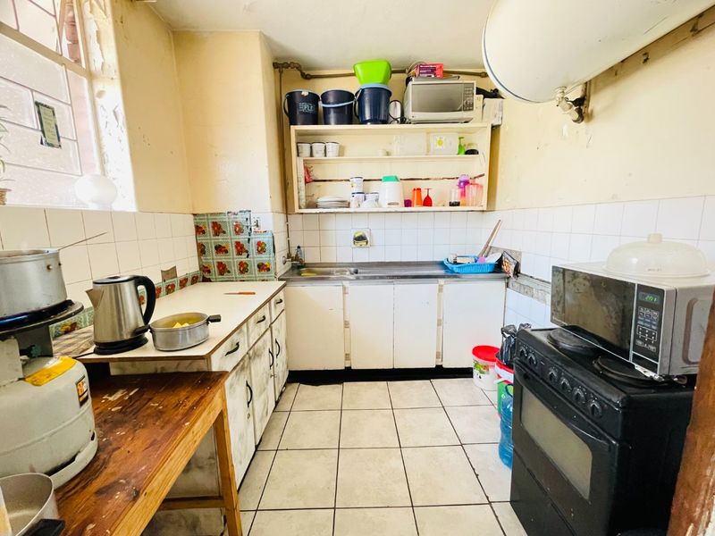 A compact kitchen featuring tiled flooring, a stainless steel sink, and built-in cabinetry, currently requiring significant cosmetic updates and maintenance.