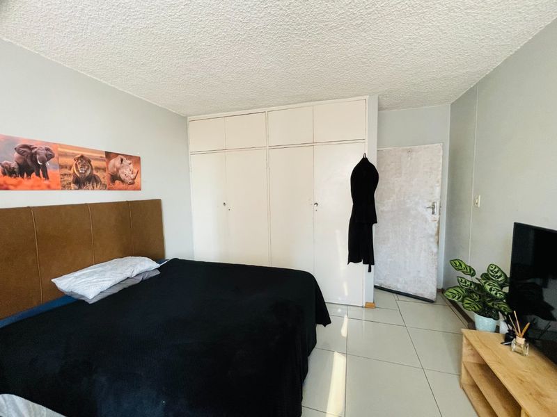A bedroom featuring tiled flooring, a textured ceiling, and built-in cupboards providing ample storage space.