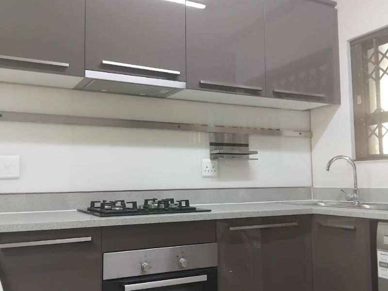 Modern kitchen featuring high-gloss cabinetry, stone countertops, a built-in oven, gas hob, and a sleek glass splashback.