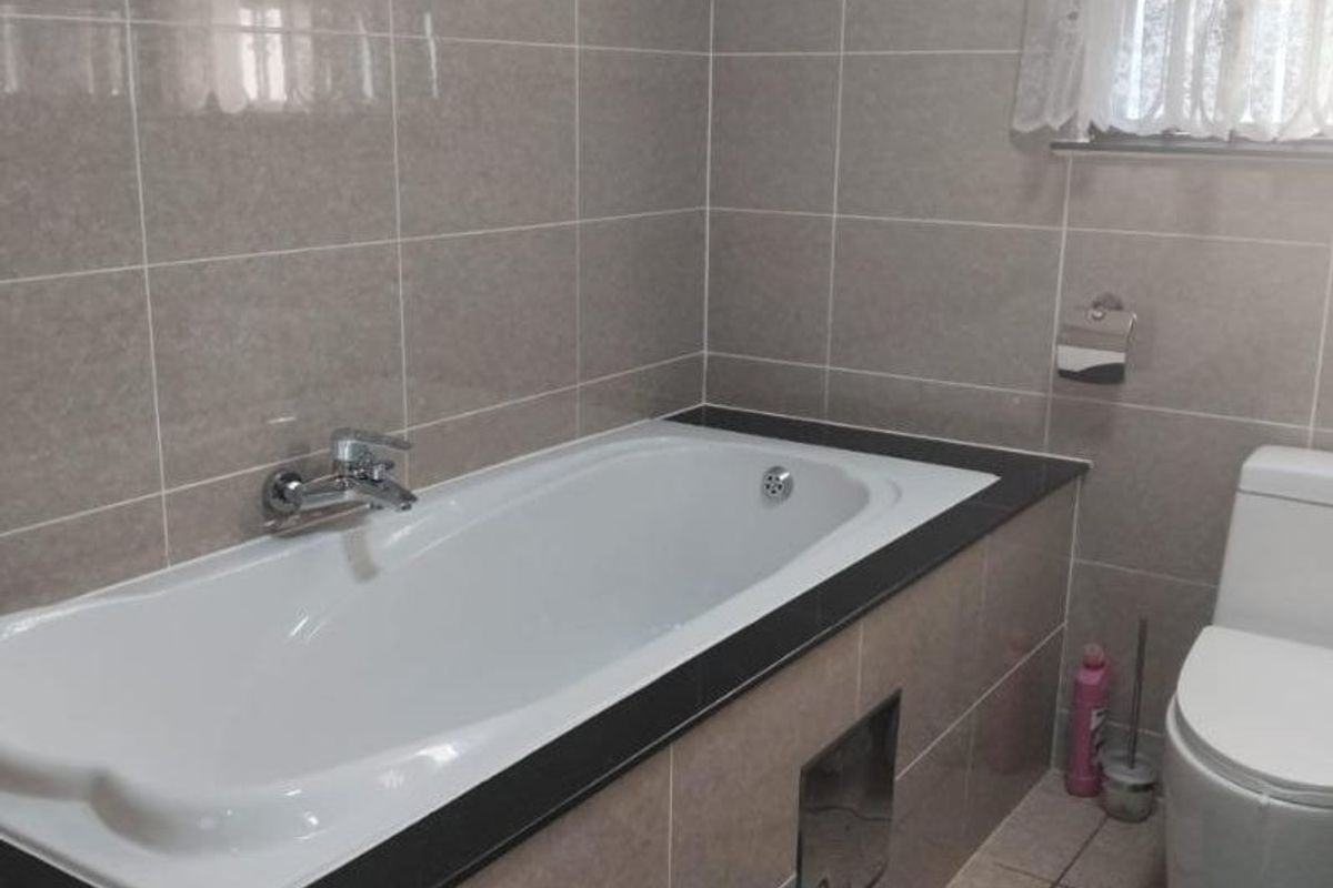 A clean, tiled bathroom featuring a built-in bathtub with a dark surround and a modern toilet.
