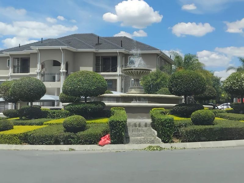 A well-maintained apartment complex exterior featuring a central decorative fountain and manicured garden landscaping in the front courtyard.