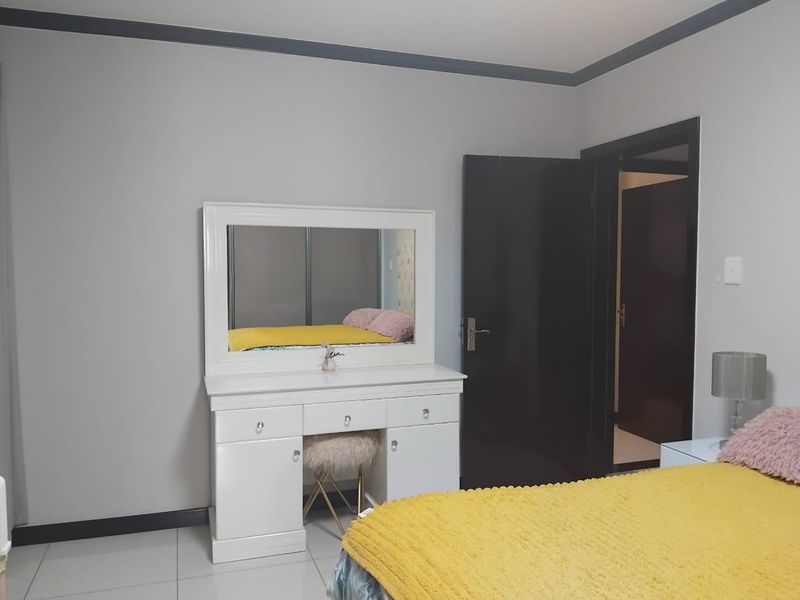 A well-maintained bedroom featuring neutral wall tones, dark door frames, tiled flooring, and built-in cupboard storage.