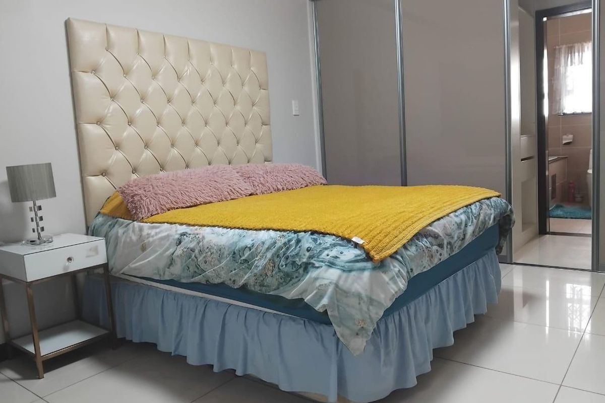 A well-maintained bedroom featuring tiled flooring and a large built-in sliding door wardrobe, with direct access to an en-suite bathroom.