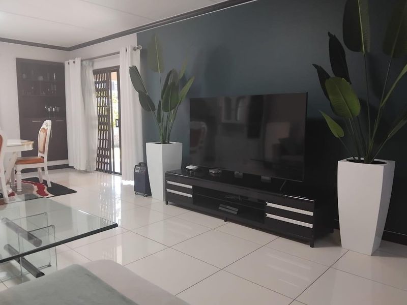 A bright living room featuring polished tiled flooring, a dark accent wall, and a sliding glass door providing access to the outdoor area.