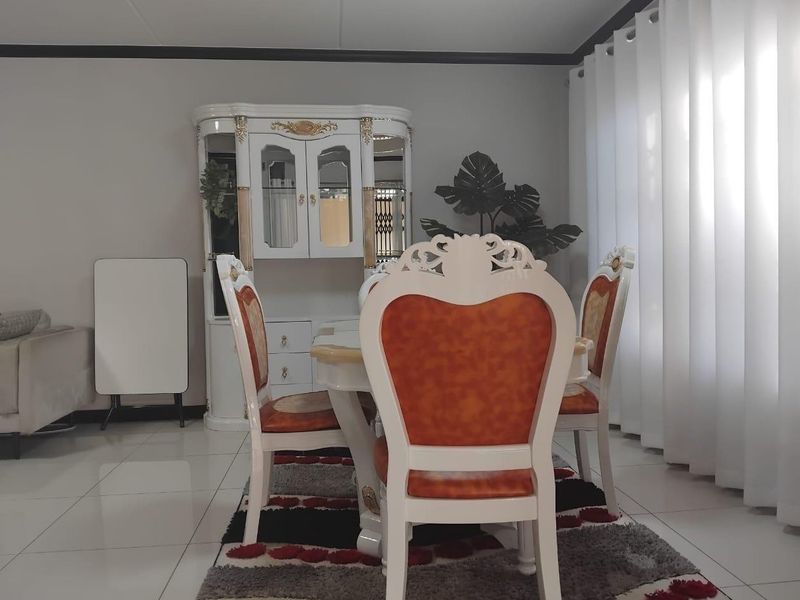 A bright dining area featuring polished tiled flooring and large windows with curtains, providing a clean and functional space for meals.