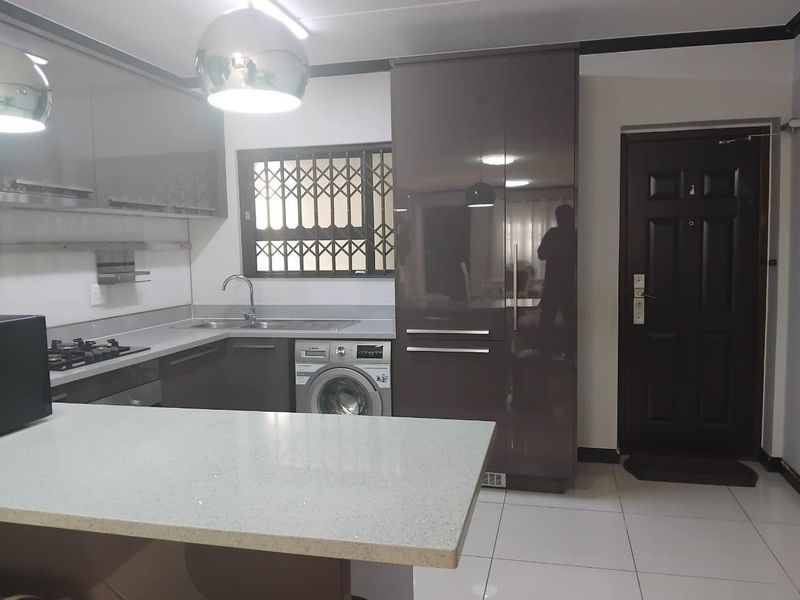 Modern kitchen featuring high-gloss cabinetry, stone countertops, a gas hob, and an integrated washing machine, with direct access to the entrance.