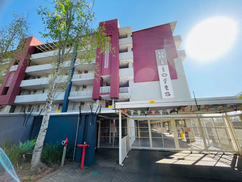 Front elevation of the Uni Lofts apartment complex featuring a secure gated entrance, paved driveway, and multi-level balconies.