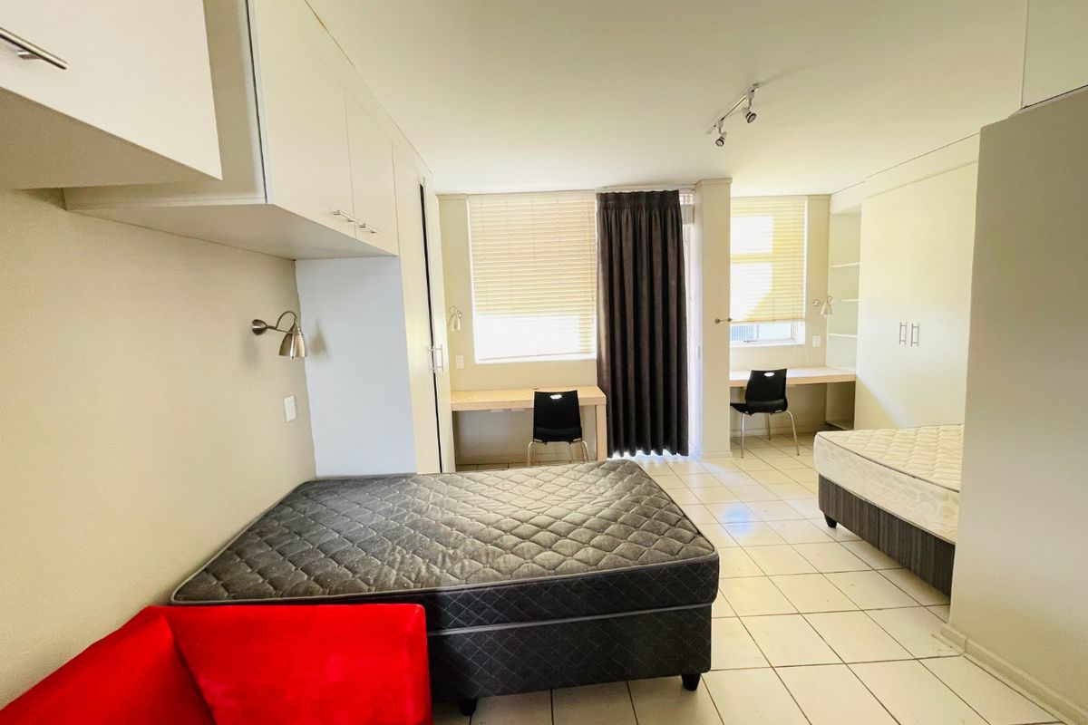 Spacious bedroom featuring built-in cupboards, dual built-in desks, tiled flooring, and large windows with venetian blinds for natural light.