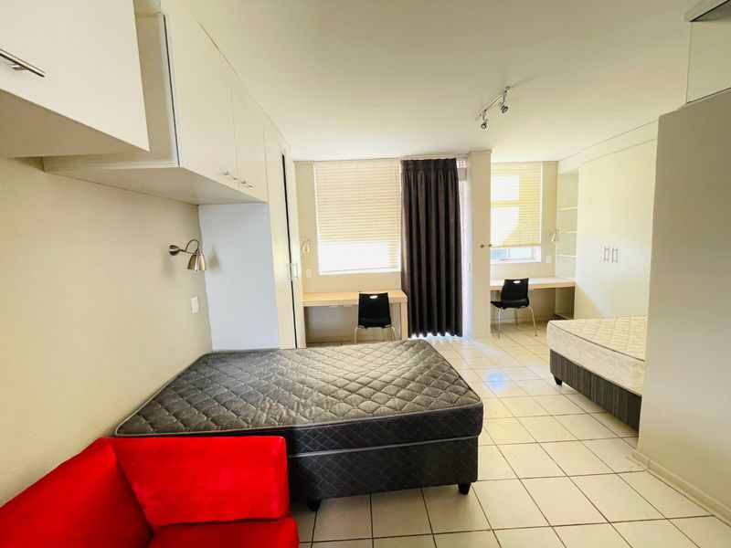 Spacious bedroom featuring built-in cupboards, dual built-in desks, tiled flooring, and large windows with venetian blinds for natural light.