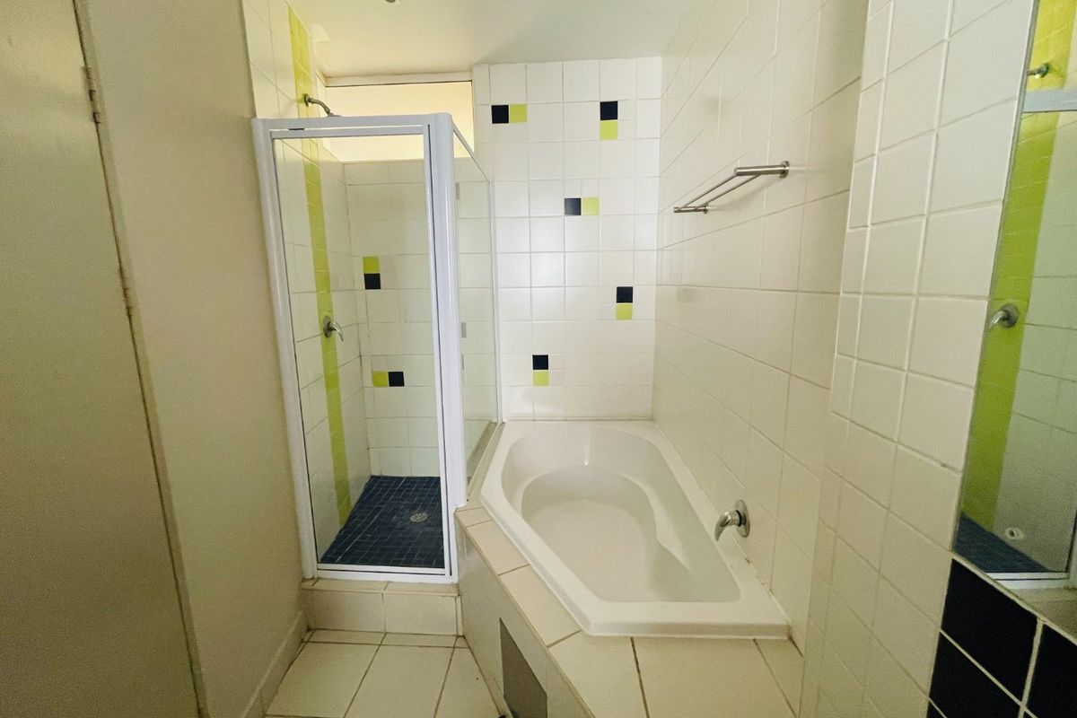 A functional bathroom featuring a built-in bathtub, separate shower enclosure, and tiled finishes throughout.