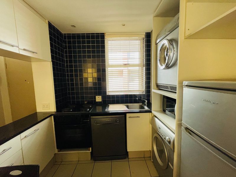 Compact kitchen featuring dark tiled backsplash, black granite countertops, built-in oven and hob, and integrated laundry appliances in a functional layout.