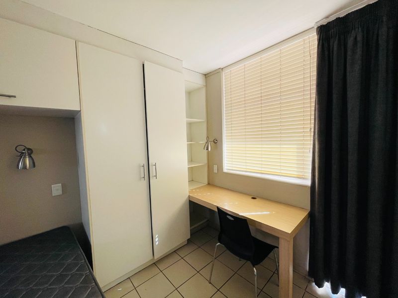 A functional bedroom featuring built-in cabinetry, a dedicated desk area with shelving, tiled flooring, and window treatments.