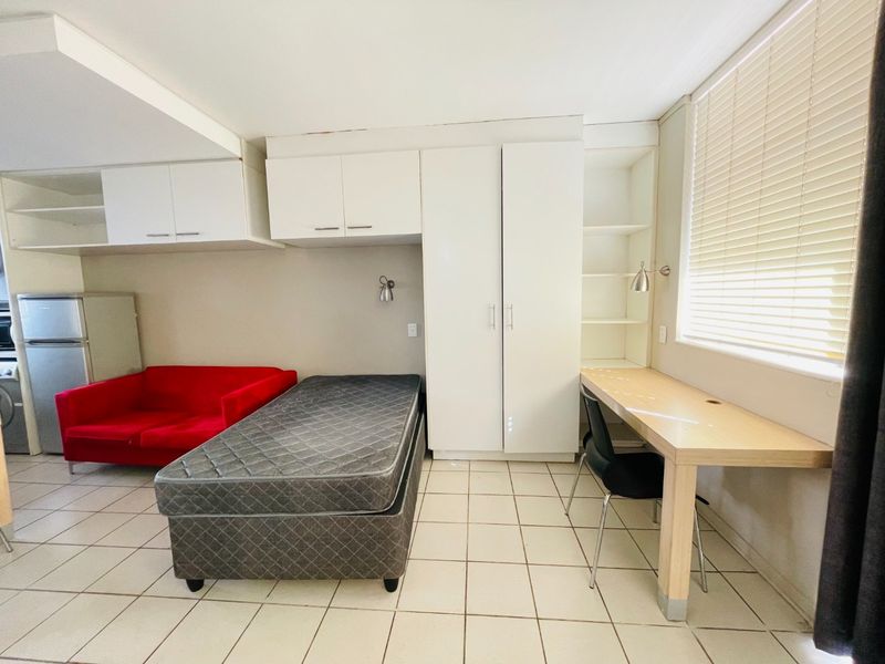 A functional bedroom featuring built-in cupboards, overhead storage, a dedicated desk area, and tiled flooring, offering practical storage and workspace solutions.