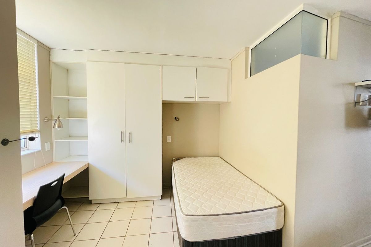 A functional bedroom featuring built-in cabinetry, a desk area, tiled flooring, and a transom window for natural light.