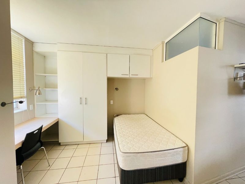 A functional bedroom featuring built-in cabinetry, a desk area, tiled flooring, and a transom window for natural light.