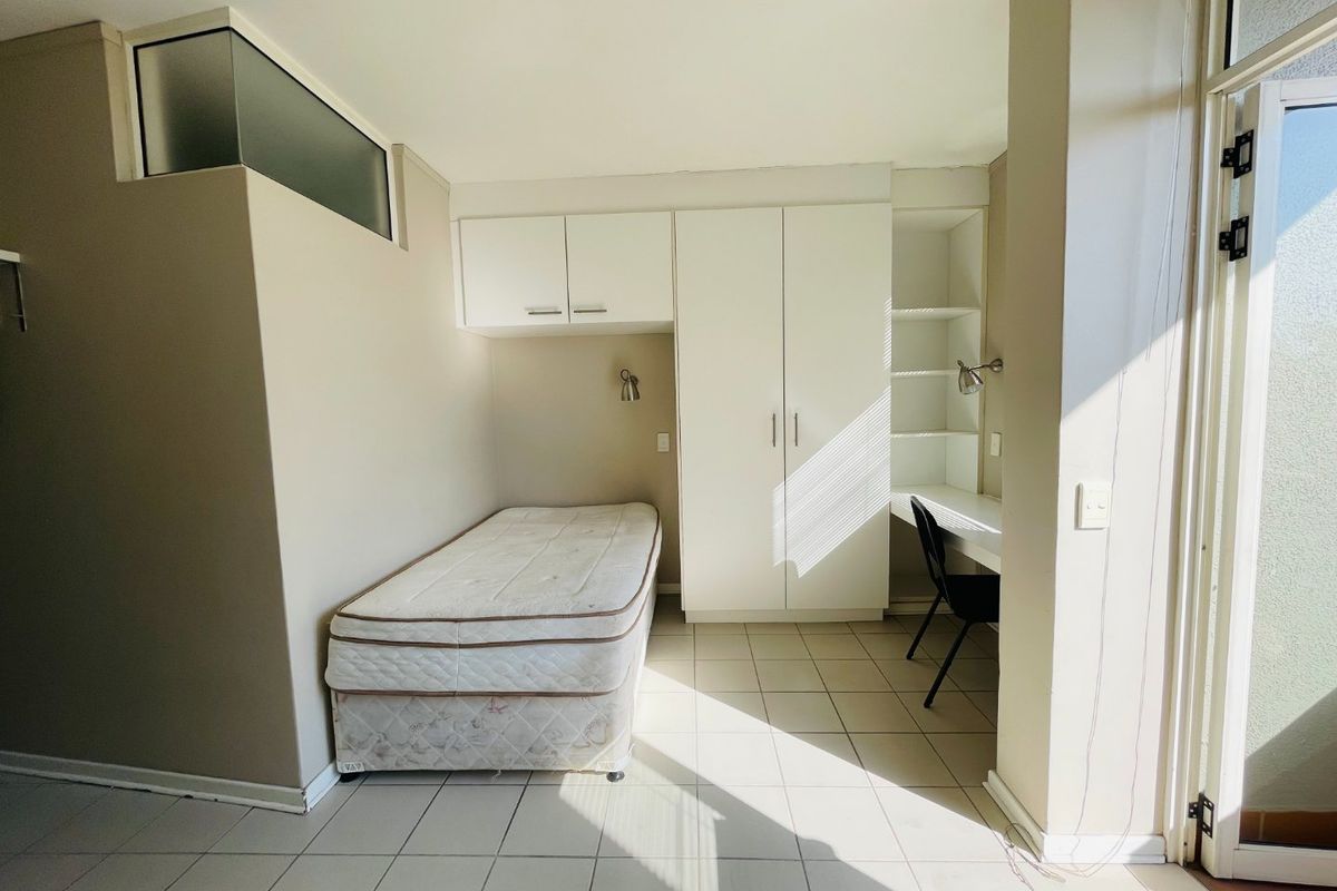 A functional bedroom featuring built-in cabinetry, a desk area, tiled flooring, and a transom window providing natural light.